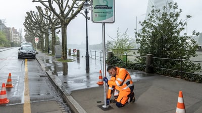 Arbeiter in orangefarbener Kleidung repariert Strassenschild bei regnerischem Wetter.