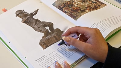 Person markiert Text in einem Kunstbuch mit einer Statue und Gemälde.