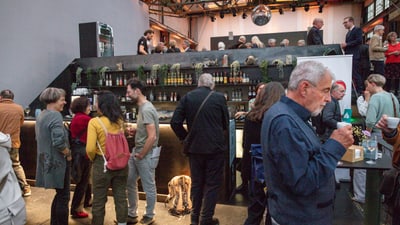 Menschen unterhalten sich in einer Bar mit Pflanzen und Getränken in Regalen.