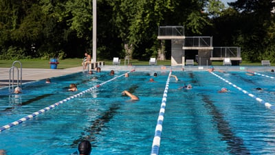 Schwimmer in einem Freibad mit Startblöcken und Sprungbrett.