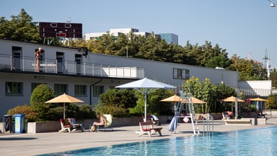 Aussenpoolbereich mit Sonnenliegen und Sonnenschirmen neben einem Gebäude.