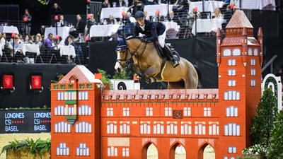 Reiter springt mit Pferd über Hindernis bei einem Turnier in der Halle.",