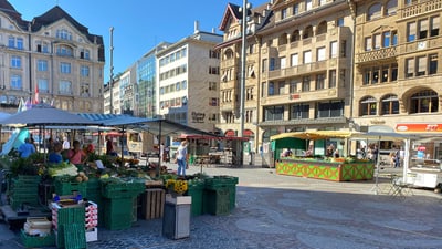 Marktstände auf einem Stadtplatz mit historischen Gebäuden im Hintergrund.