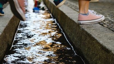 Beine mit Sneakers über Wasserkanal auf Gehwegkante.