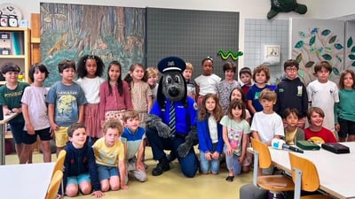 Gruppe von Kindern mit einem Maskottchen in einem Klassenzimmer.