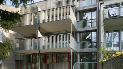 Mehrstöckiges Gebäude mit Balkonen und roten Fensterrahmen.
