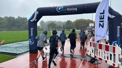 Läufer im Regen beim Zieleinlauf auf der Rennstrecke.
