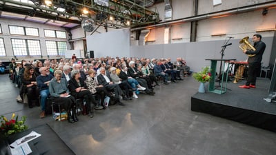 Musiker spielt Horn vor Publikum in Industriehalle.