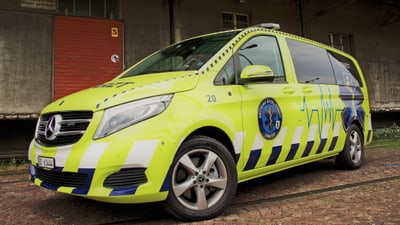 Gelber Notarztwagen mit Sanitätslogo auf einem Pflasterweg vor einem Gebäude.