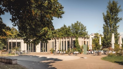 Moderne Café-Terrasse mit Bäumen und Sonnenschirmen.