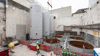 Bauarbeiter an einem Baustellenbereich mit grossen zylindrischen Tanks.