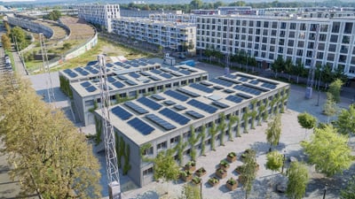 Drei zweistöckige rechteckige Gebäude mit Flachdach und Solarmodulen darauf.