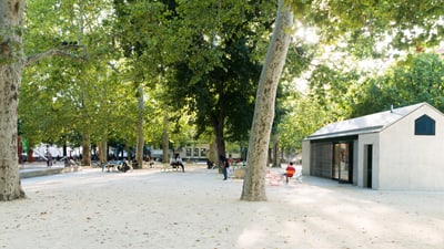 Park mit Bäumen, kleinem Gebäude und Personen im Freien.