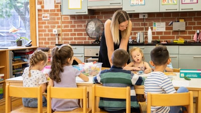 Gruppe von Kindern, die an einem Tisch mit einer Lehrerin sitzen.