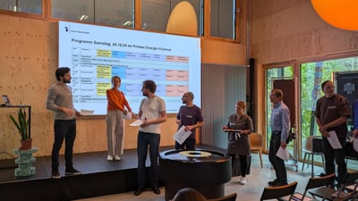 Menschen präsentieren vor einer Projektionswand in einem Raum mit Holzverkleidung.