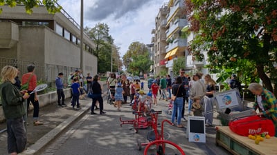 Menschen auf einer belebten Strasse mit Aktivitäten und Ständen im Freien.