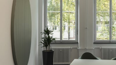 Büro mit Tisch, Stuhl, Pflanze, grossem Fenster und Wandkunst.