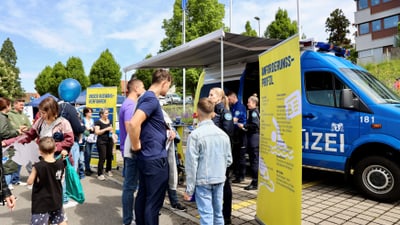 Menschen bei einer Polizeiveranstaltung neben einem blauen Einsatzfahrzeug.