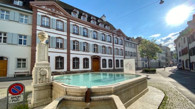 Historisches Gebäude mit Brunnen und ruhiger Strasse bei Tageslicht.