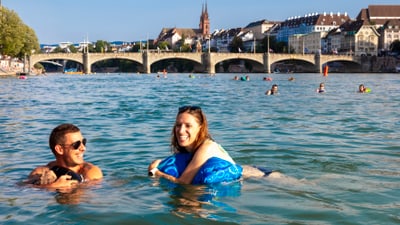 Menschen schwimmen im Fluss mit einer Brücke und Stadt im Hintergrund.