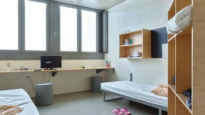 Einfach eingerichtetes Zimmer mit zwei Betten und einem Schreibtisch.