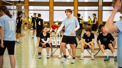 Jugendliche spielen Hallenvolleyball mit Punktetafel.",