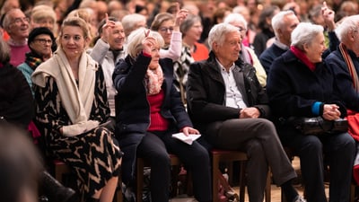 Menschen sitzen und heben die Hand während einer Veranstaltung.