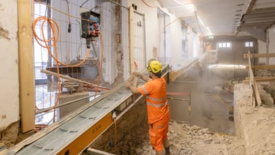 Person in oranger Arbeitskleidung auf Baustelle mit Förderband.