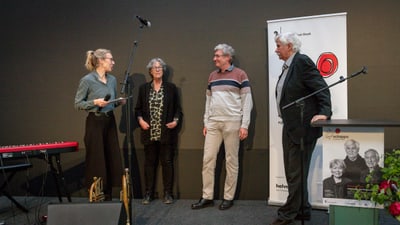 Vier Personen auf einer Bühne bei einer Veranstaltung mit Mikrofon und Keyboard.