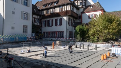 Arbeiter führen Bauarbeiten in einem Innenhof mit historischen Gebäuden im Hintergrund durch.