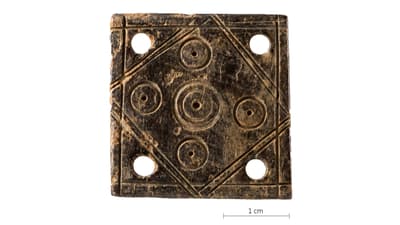 Quadratisches frümittelalterliches Webbrettchen aus Hirschgeweih, gemustert mit Kreisen und Linien und in den  Ecken runde Löcher, Massstab 1 cm.