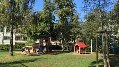 Spielplatz mit Rutsche und Holzhütten im Park.