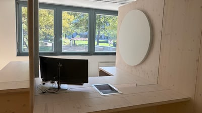 Moderner Raum mit grosser Holzschreibtischplatte, Akustikpanels und Fenstern.