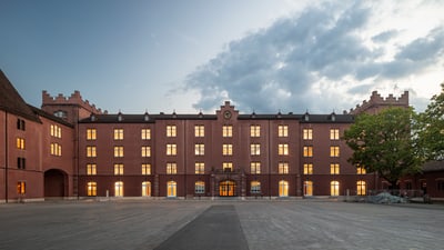 Östliche Fassade der Kaserne. Abenddämmerung und Licht dringt durch die Fenster des grossen rötlichen Gebäude.