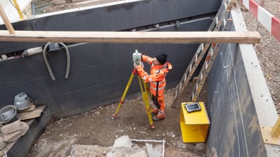 Archäologin mit Vermessungsgerät in Grube auf Ausgrabung.