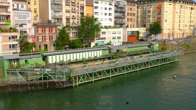 Der Rhein mit dem Steg und Garderobenhäuschen des Rheinbads und dahinter die Wohnhäuser am Rheinufer.