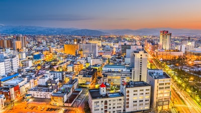 Luftaufnahme der Stadt Toyama/Japan bei Sonnenuntergang mit beleuchteten Gebäuden.