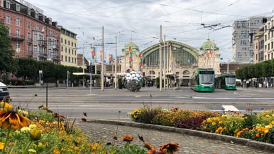 Blumenbeet und Strassenbahn vor einem Bahnhof.