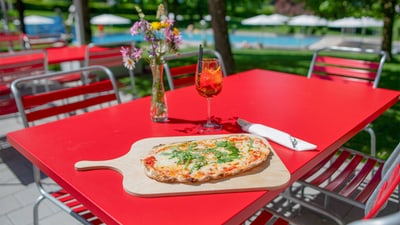 Pizza und Getränk auf rotem Tisch im Freien.