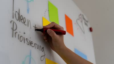 Hand schreibt auf Whiteboard mit Haftnotizen.