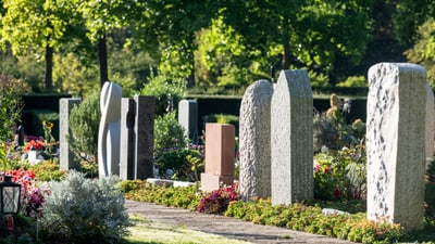 Grabsteine auf einem sonnigen Friedhof mit Grünanlage.