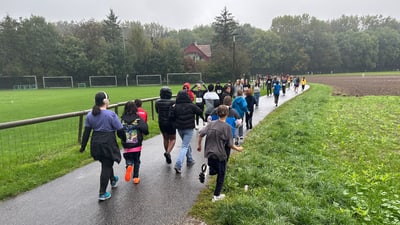 Gruppe von Kindern joggt auf einem Weg neben einem Fussballplatz im Freien.