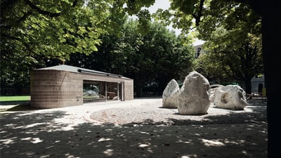 Pavillon und davor 3 grosse Steinbrocken, rundherum Bäume, die Schatten werfen.