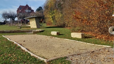 Spielplatz mit Boulebahn und im Hintergrund sichtbarer Kletterwand und Haus im Herbst.