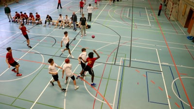 Kinder spielen Basketball in einer Turnhalle.
