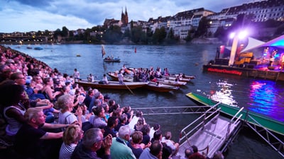 People sit on the banks of the Rhine and listen to the concerts on the raft.