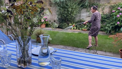 Eine Frau giesst den Garten neben einem gedeckten Tisch.