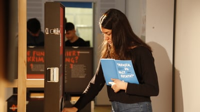 Jugendliche mit einem Leitfaden in der Hand, die ein Ausstellungsstück anfasst.