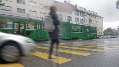 Person bei Regen auf Zebrastreifen, grüner Strassenbahn im Hintergrund."  