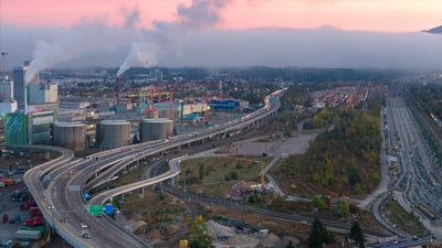 Industrieanlage und Autobahn bei Sonnenuntergang, mit Rauch aus Schornsteinen und Nebel.